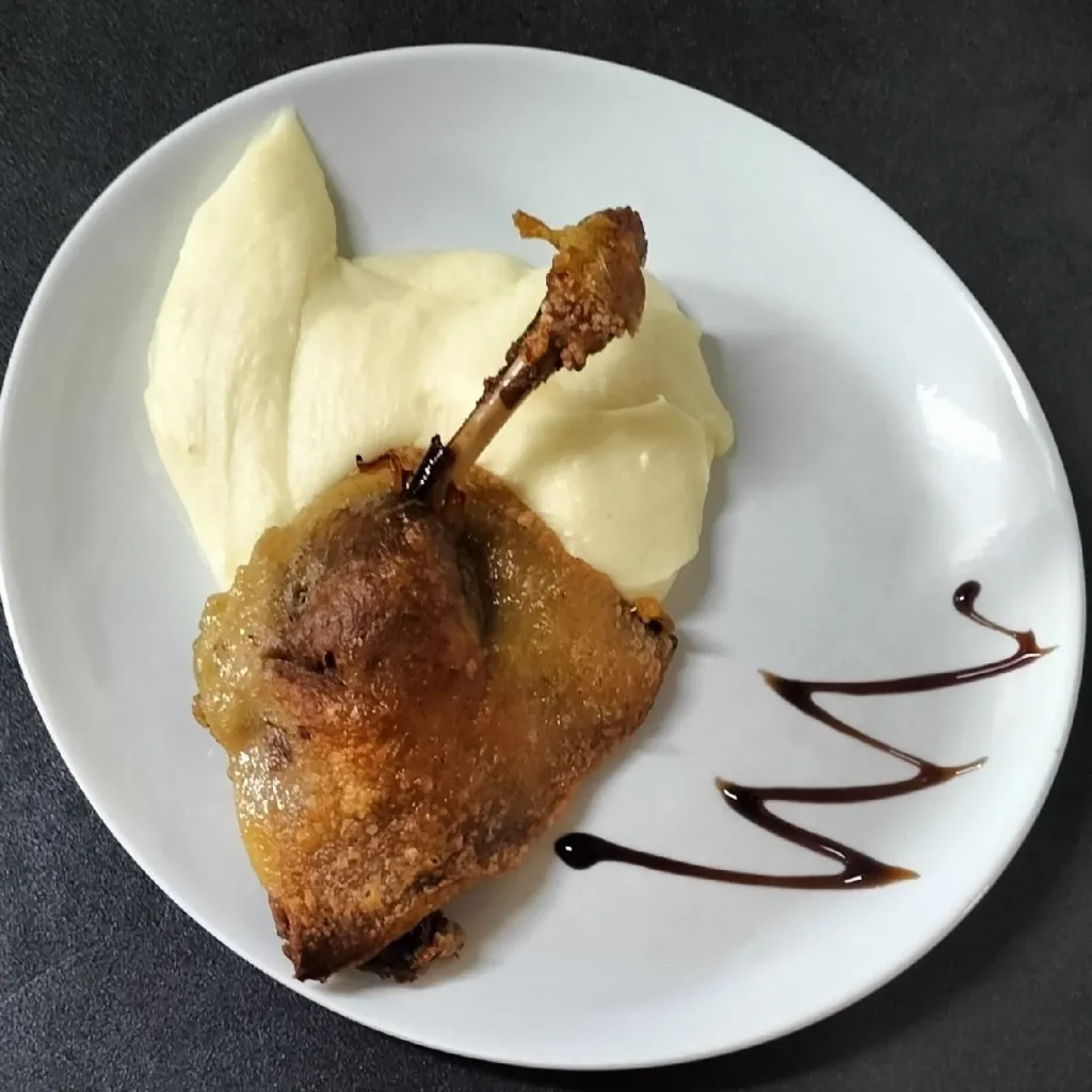 Cuisse de confit de canard doré sur une purée de pommes de terre, avec un trait de sauce brune, vue de dessus