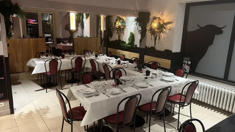 Salle du restaurant avec une longue table dressée de nappes blanches, de verres et de chaises rouges et noires