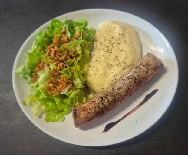Saucisse grillée sur une purée d’aligot poivrée, avec salade verte et oignons frits