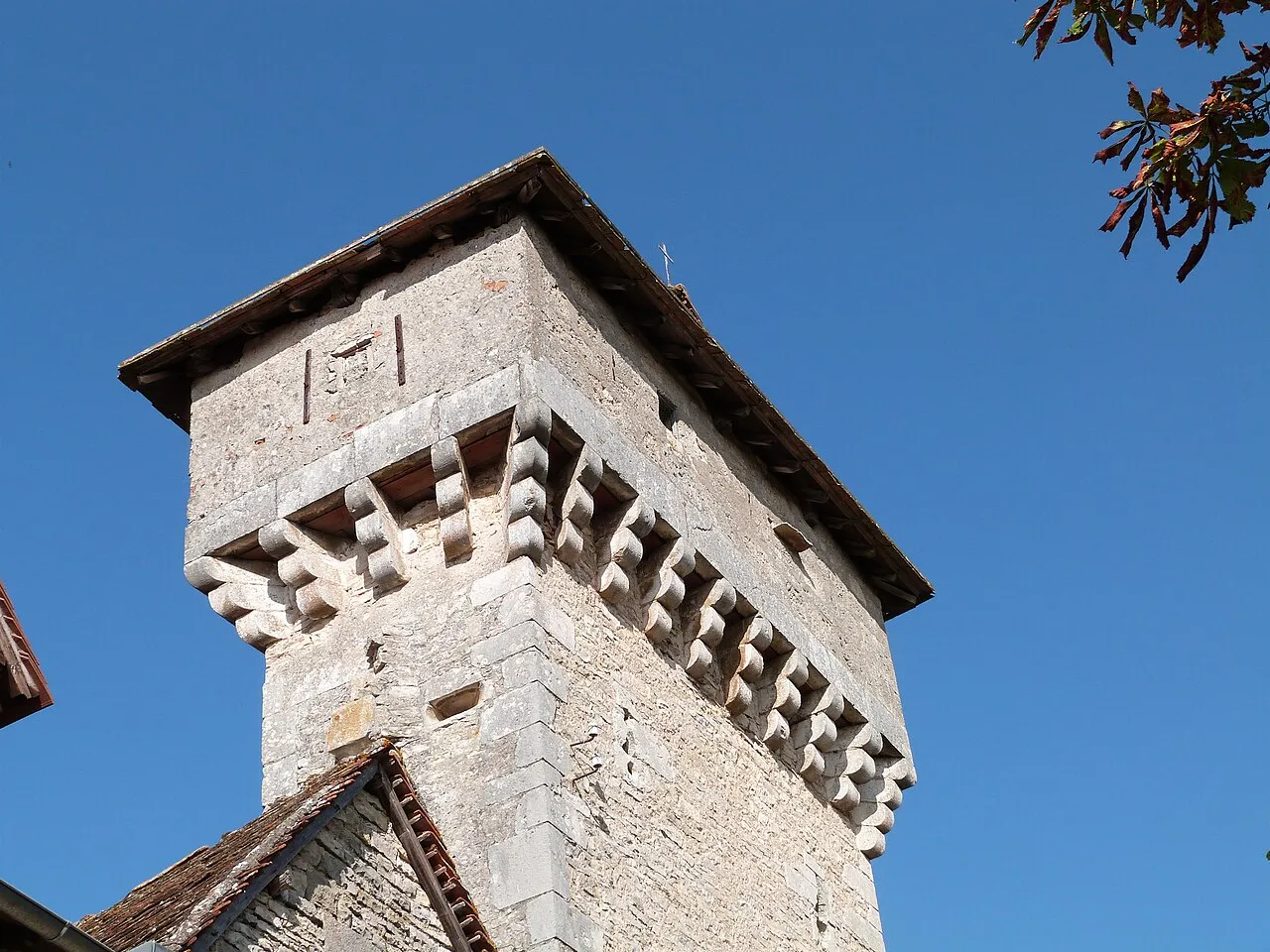 Haut de la tour de Cardalhac à Villeneuve-d’Aveyron, en pierre claire avec ses mâchicoulis sous un ciel bleu