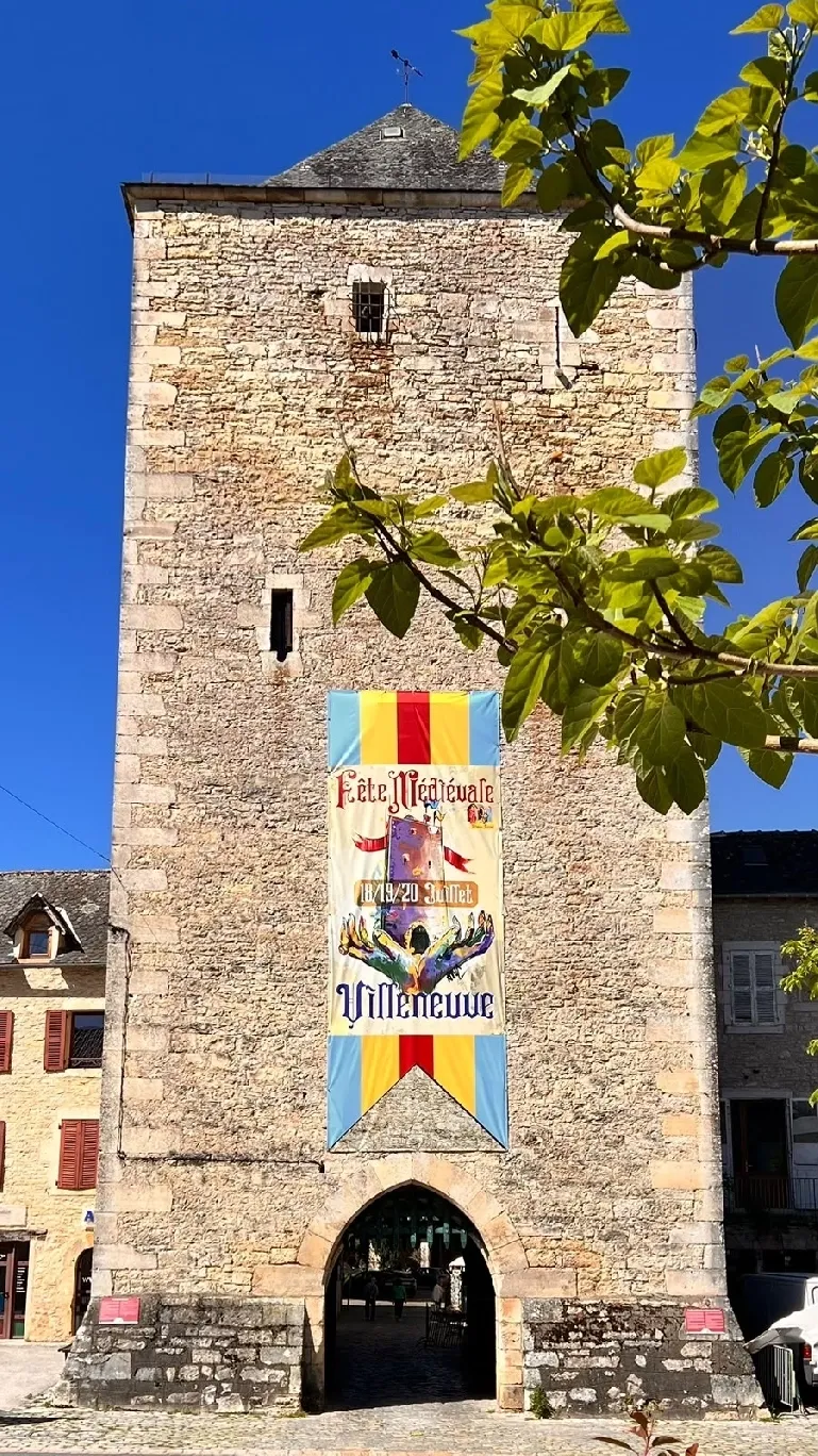 Tour Soubirane en pierre dorée, avec son passage voûté et une bannière de fête médiévale, sous un ciel bleu