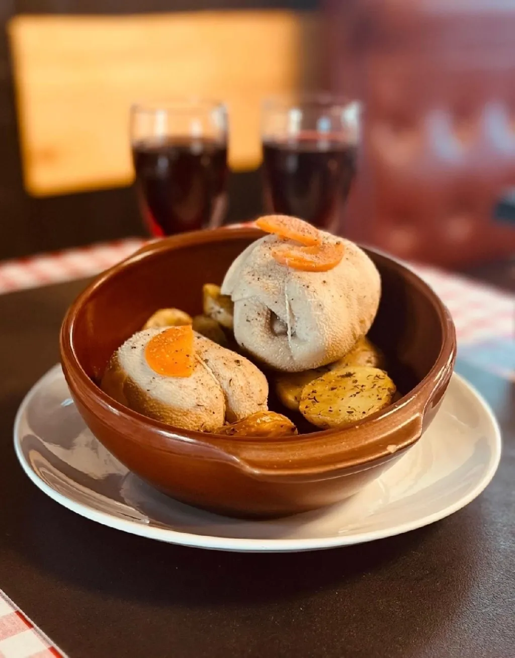 Tripoux et pommes de terre dans un plat en terre cuite, avec deux verres de vin rouge
